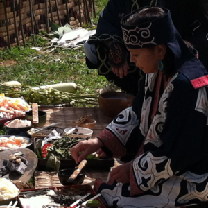 Image of an Ainu woman sitting on a mat outdoors