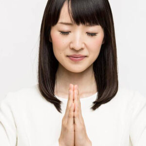A close-up photo of Marie Kondo with eyes closed, head slightly bowed, and palms clasped together