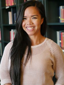 Headshot of Ruby in front of book shelves, white knit sweater